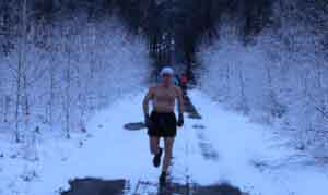Mężczyzna biegnący w krótkich spodenkach, bez koszulki, leśną ścieżką pokrytą śniegiem