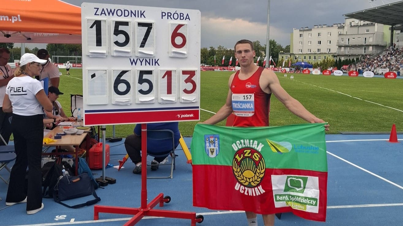 Młody sportowiec pozujący z flagą przy tablicy wyników