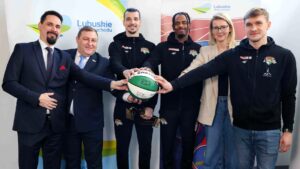 Sześć uśmiechniętych osób z dłońmi na piłce do koszykówki