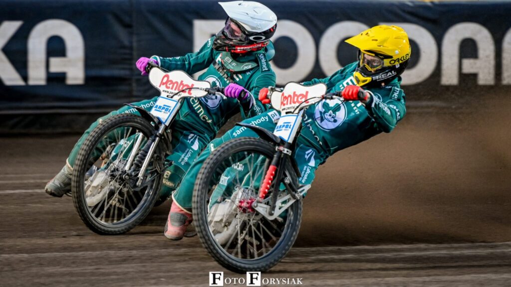 Dwie osoby jadące na motocyklach żużlowych