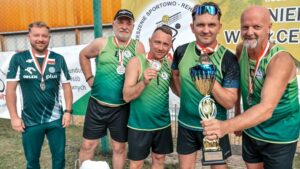 Pięciu mężczyzn w sportowych strojach, z medalami i pucharem