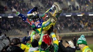 Zawodnik w sportowym stroju i kasku, podrzucany przez kolegów